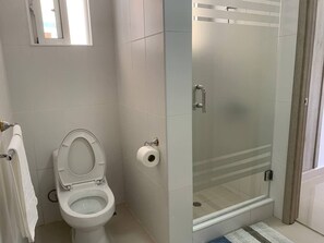 Un baño con inodoro, cabina de ducha de vidrio y perchero para toallas.