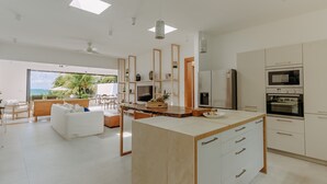 Cocina moderna con armarios blancos, una isla central y vistas al océano a través de amplios ventanales.