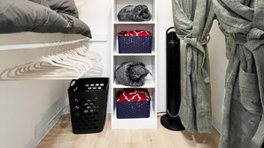 Ein schmaler begehbarer Kleiderschrank mit Kleiderstange, Regalen voller gefalteter Kleidung und einem auf einem Kleiderbügel aufgehängten Bademantel.