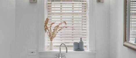 A bathroom with a white sink, a window with blinds, and two wall-mounted lights.