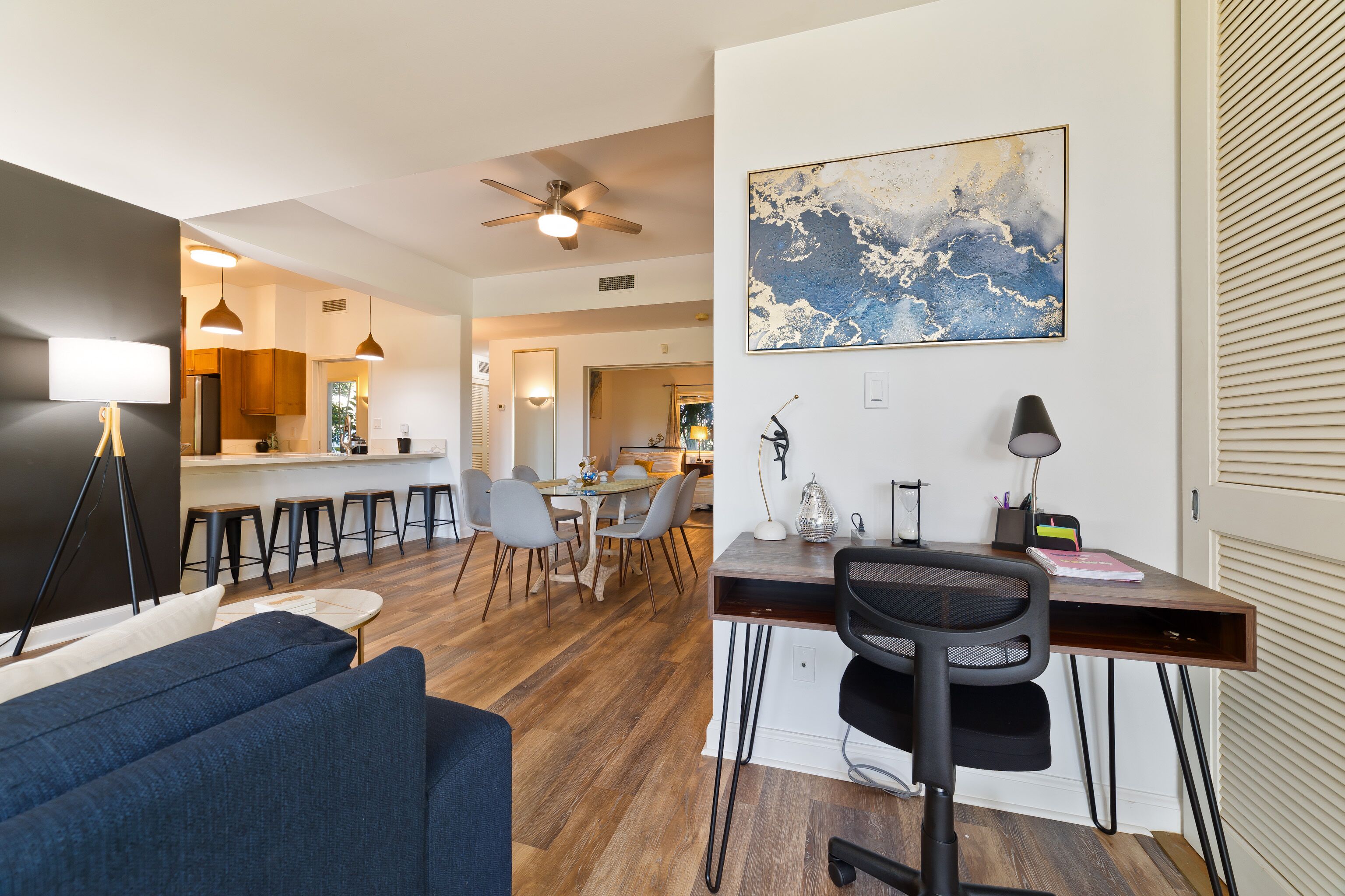 A modern living room with a sofa, a desk with a chair, and a dining area with chairs and a table.