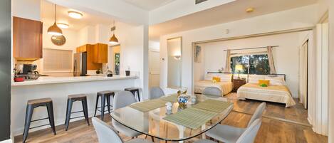 A modern kitchen with a dining area, a bedroom with a large window, and a living area with a sofa and a coffee table.