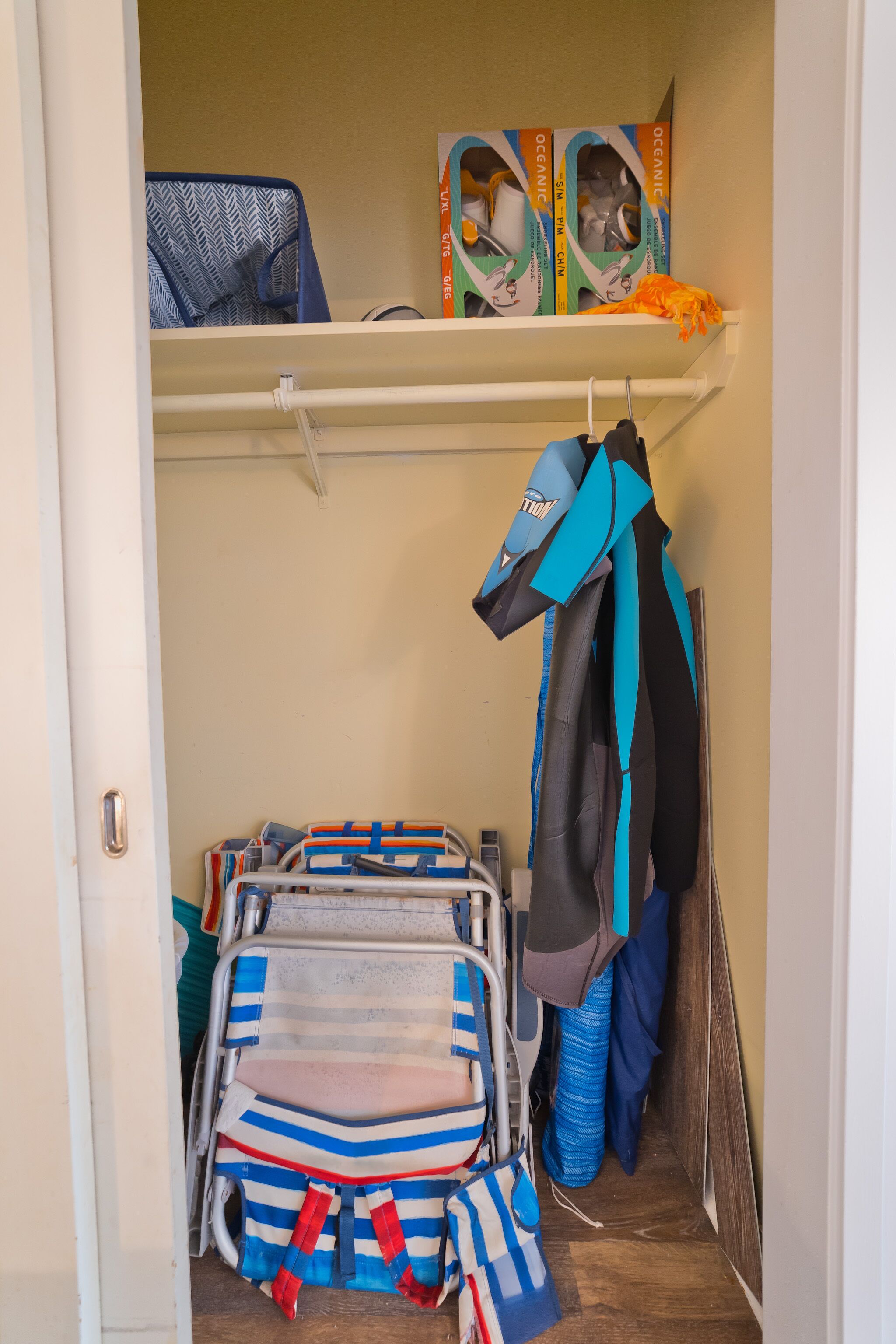 A storage area with a shelf holding boxes, a blue and white striped bag, and a blue and black jacket hanging on a hook.