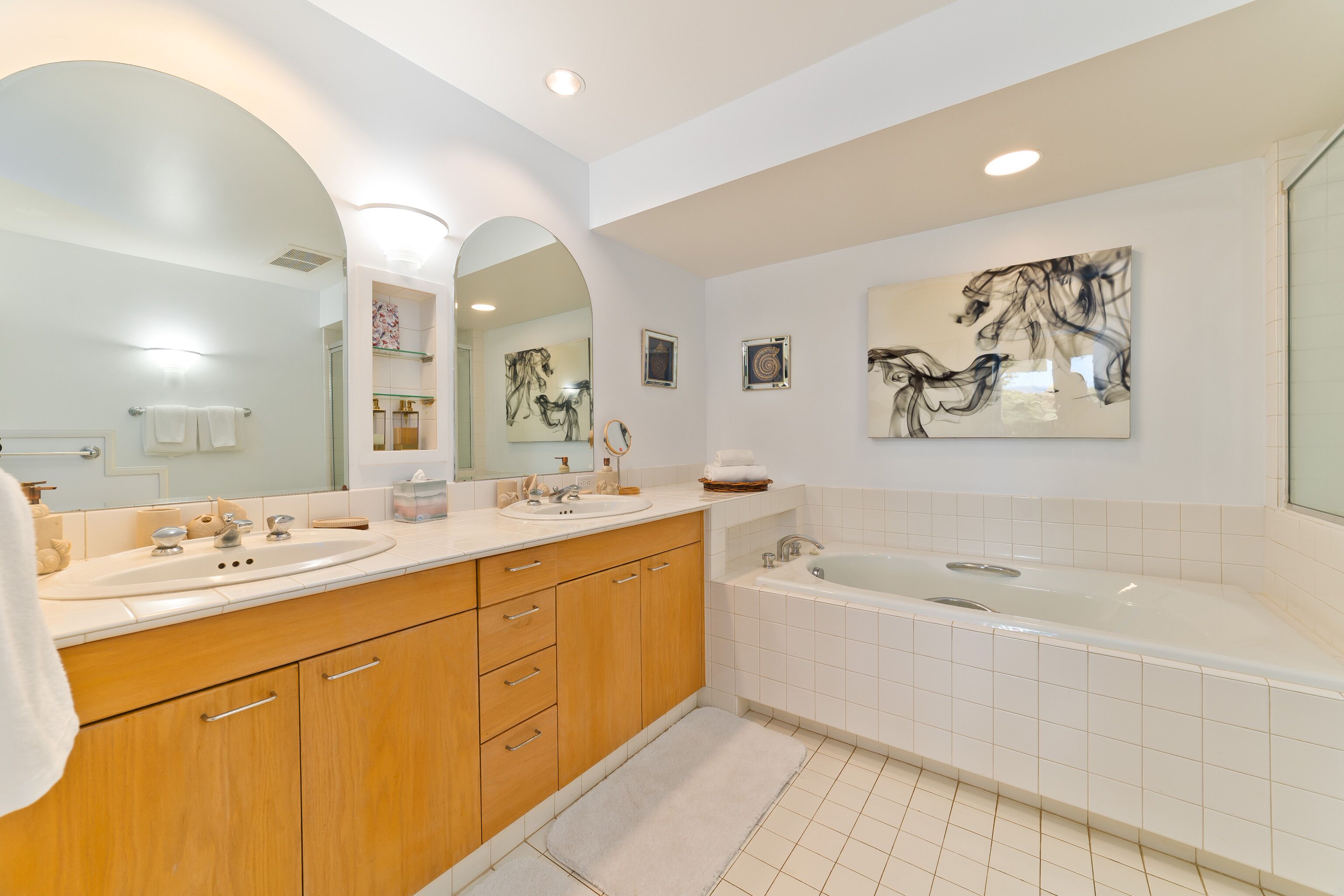 Un baño moderno con dos lavamanos, una bañera, armarios de madera y obras de arte en las paredes.