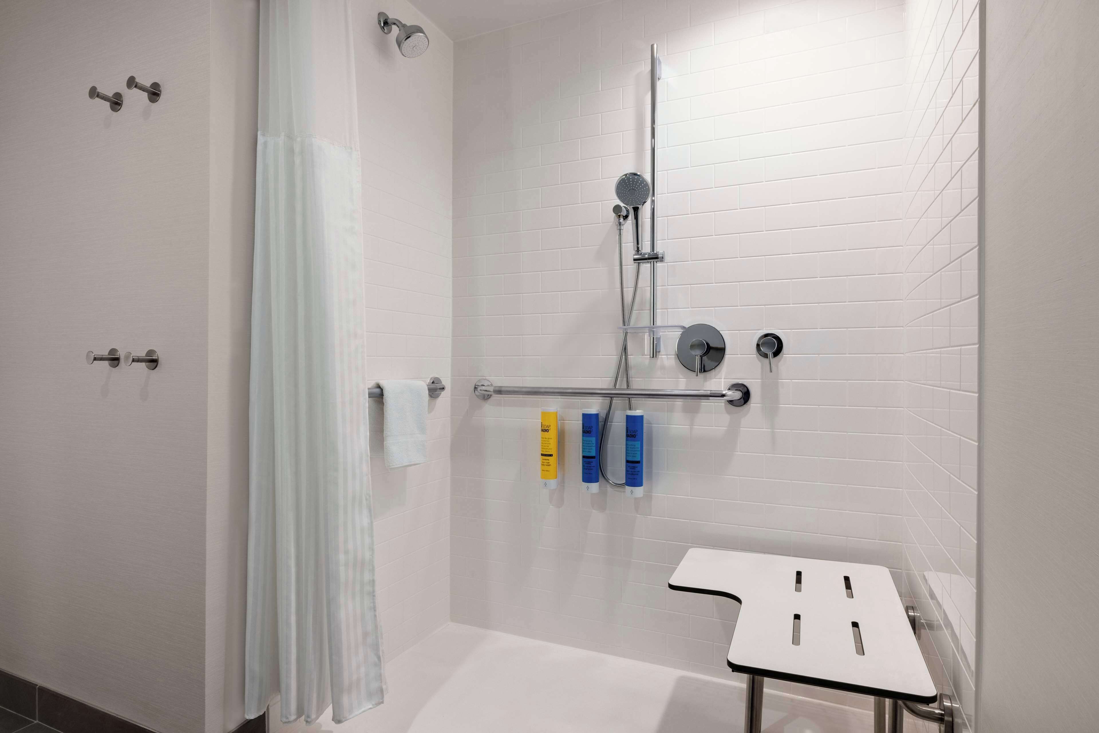 A modern bathroom with white tiled walls, a shower with a glass door, and a small white sink with a metal frame.