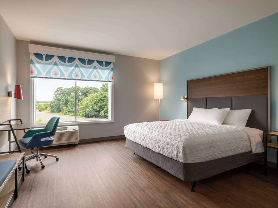 A hotel room with a large bed, a desk, a chair, and a window with a view of trees.