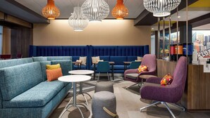 Un hall d’hôtel moderne avec un canapé bleu, des tables rondes et un comptoir d’accueil.