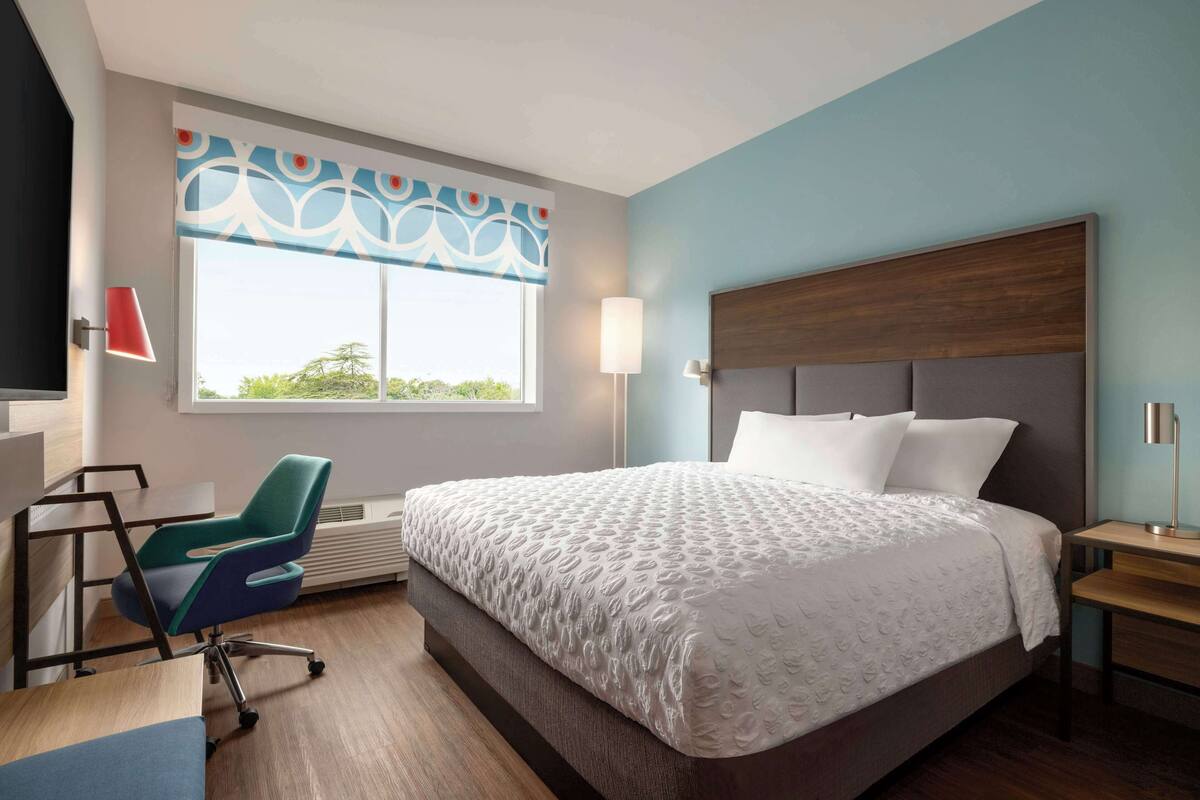 Une chambre d’hôtel avec un grand lit, un bureau, une chaise et une fenêtre donnant sur un beau paysage.