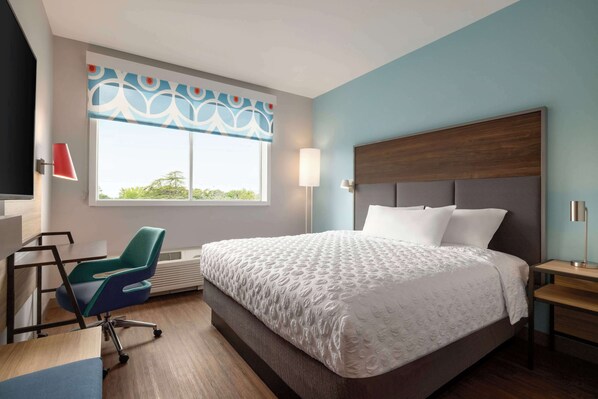 Quarto de hotel com uma cama grande, uma mesa de trabalho, uma cadeira e uma janela com vista.