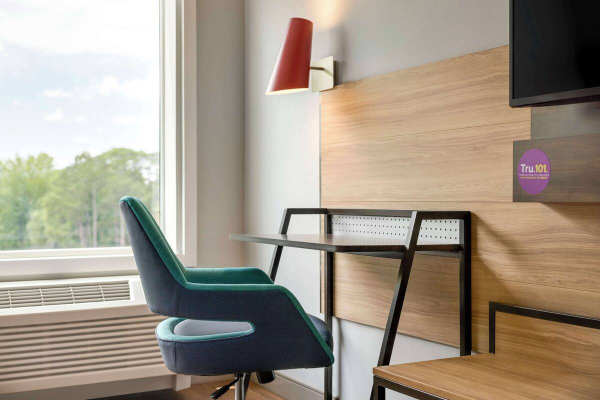Une chambre moderne avec un fauteuil turquoise, un bureau en bois et une lampe murale rouge.