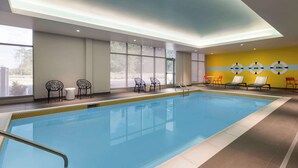 Une piscine intérieure avec des parois en verre transparent, des chaises longues et un mur jaune orné de motifs circulaires.