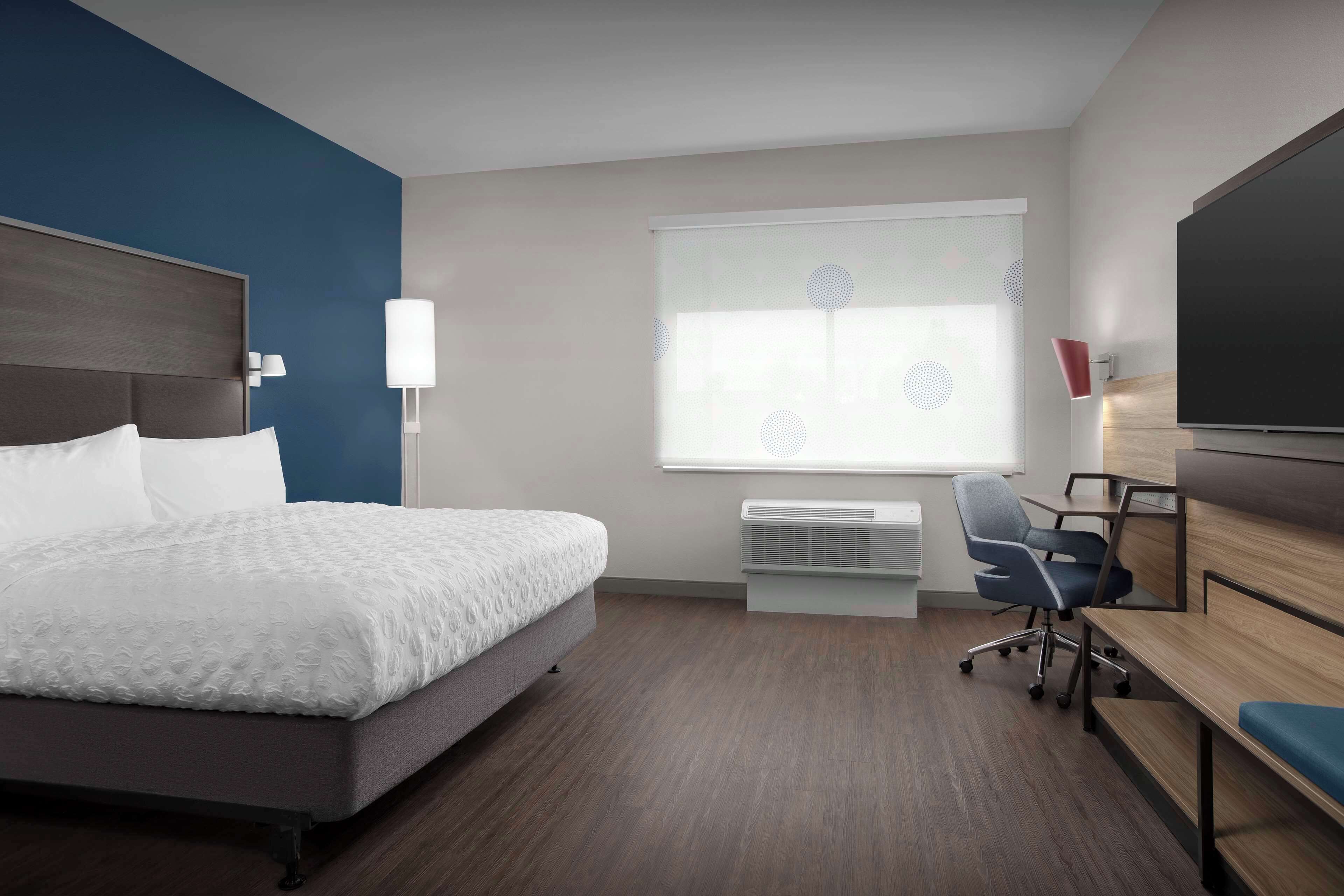 A hotel room with a bed, desk, chair, and TV.