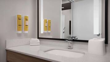 Un baño moderno con un lavamanos blanco, un espejo grande y dos artículos de tocador amarillos en la pared.