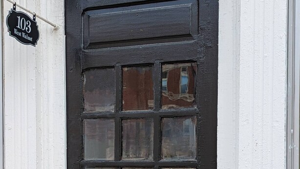 A black door with a grid pattern, a white door frame, and a small sign above the door reading "103 West Walnut". - Cozy Loft Hideaway in Robinson (Robinson)