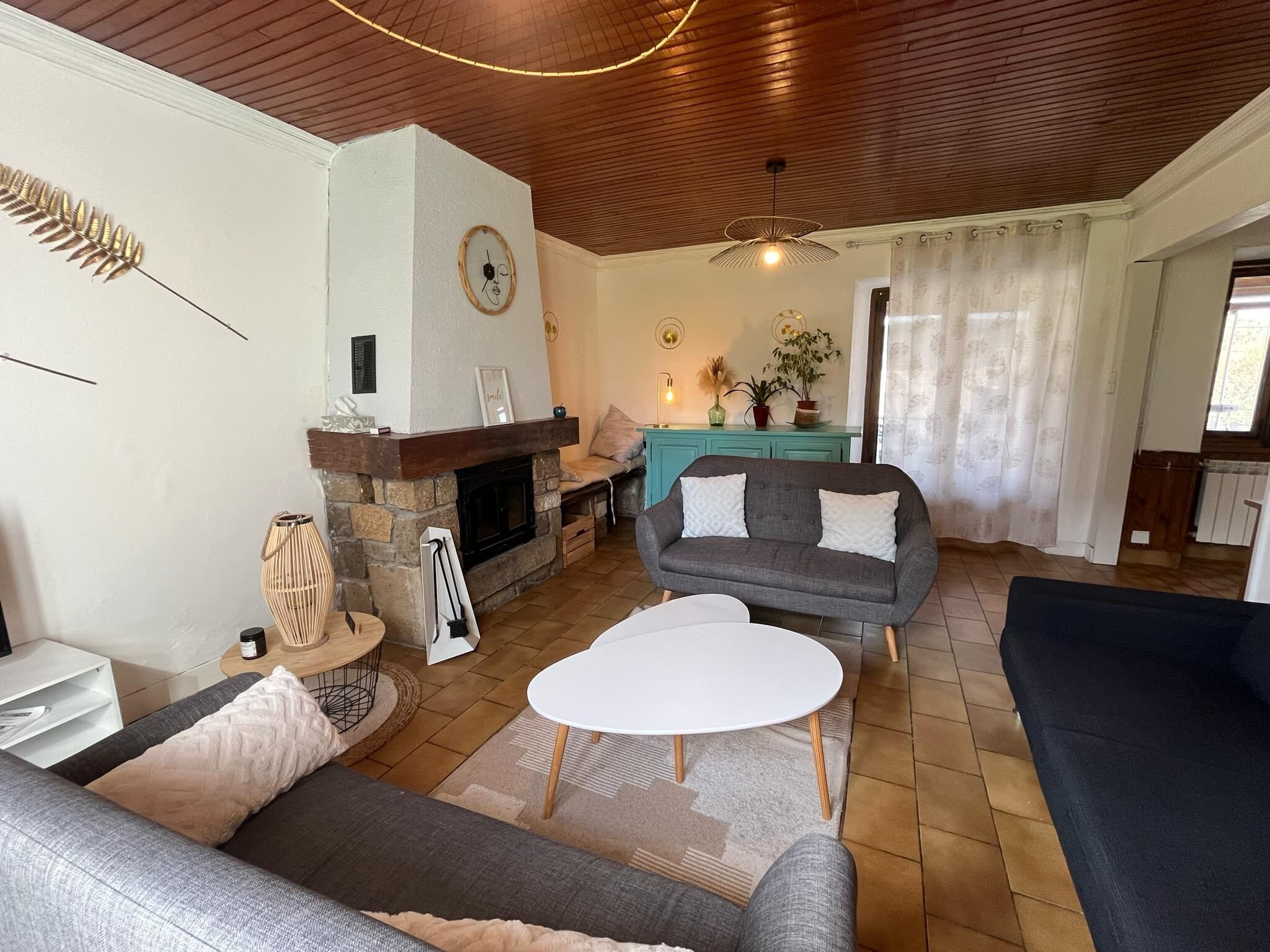 A living room with a stone fireplace, a grey sofa, a white coffee table, and a wooden ceiling.