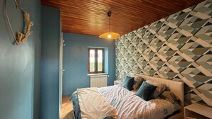 A bedroom with a bed, a window, a patterned wall, and a wooden ceiling.