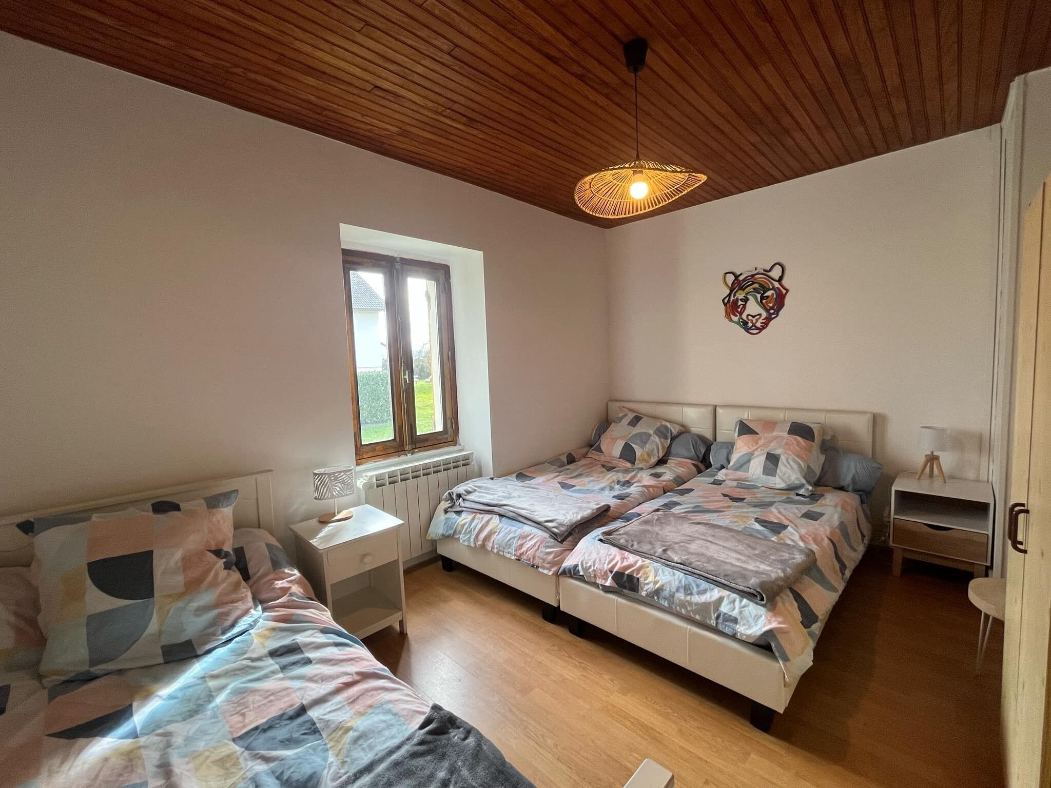 A bedroom with two beds, a window, a radiator, a wall-mounted tiger head decoration, and a hanging light fixture.