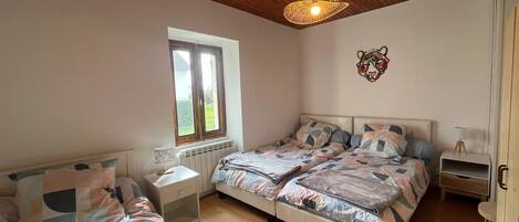 A bedroom with two beds, a window, a radiator, a wall-mounted tiger head decoration, and a hanging light fixture.