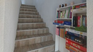 A staircase with wooden steps leading to a landing. A white bookshelf filled with books and games is on the landing.