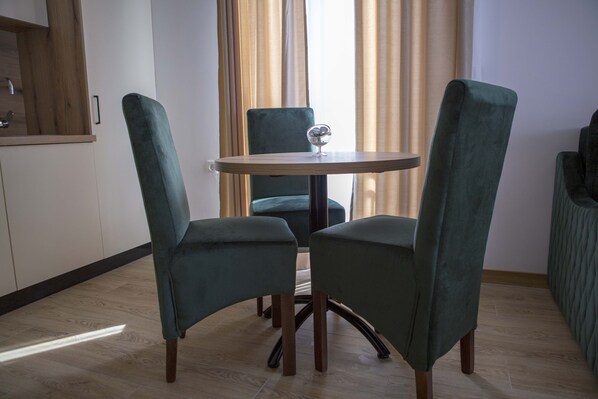 A dining area with two green upholstered chairs around a round table, a glass bowl on the table, and a wooden floor.