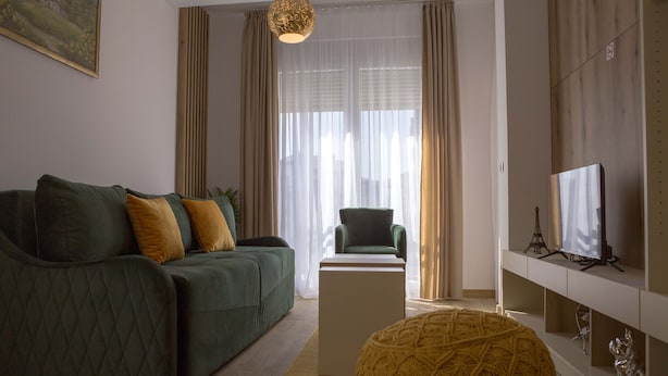 A modern living room with a green sofa, a yellow ottoman, a white coffee table, and a television on a white stand. - Apart Hotel Gondola Kolasin (Kolašin)