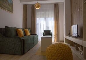 A modern living room with a green sofa, a yellow ottoman, a white coffee table, and a television on a white stand.
