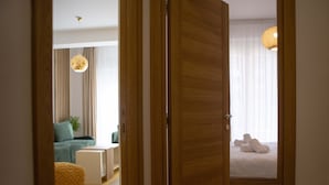 A hotel room with a wooden wardrobe, a bed with white linens, a green sofa, a small table, and a hanging light fixture. - Apart Hotel Gondola Kolasin (Kolašin)
