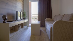 A modern room with a wooden floor, a white sofa, a small white side table, and a desk with a computer and decorative items. - Apart Hotel Gondola Kolasin (Kolašin)