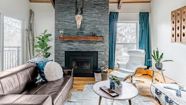 A cozy living room with a stone fireplace, leather sofa, and a white armchair. - VAIL HAUS: 2 Bedroom Penthouse + Loft on Vail Bus Route (Vail)