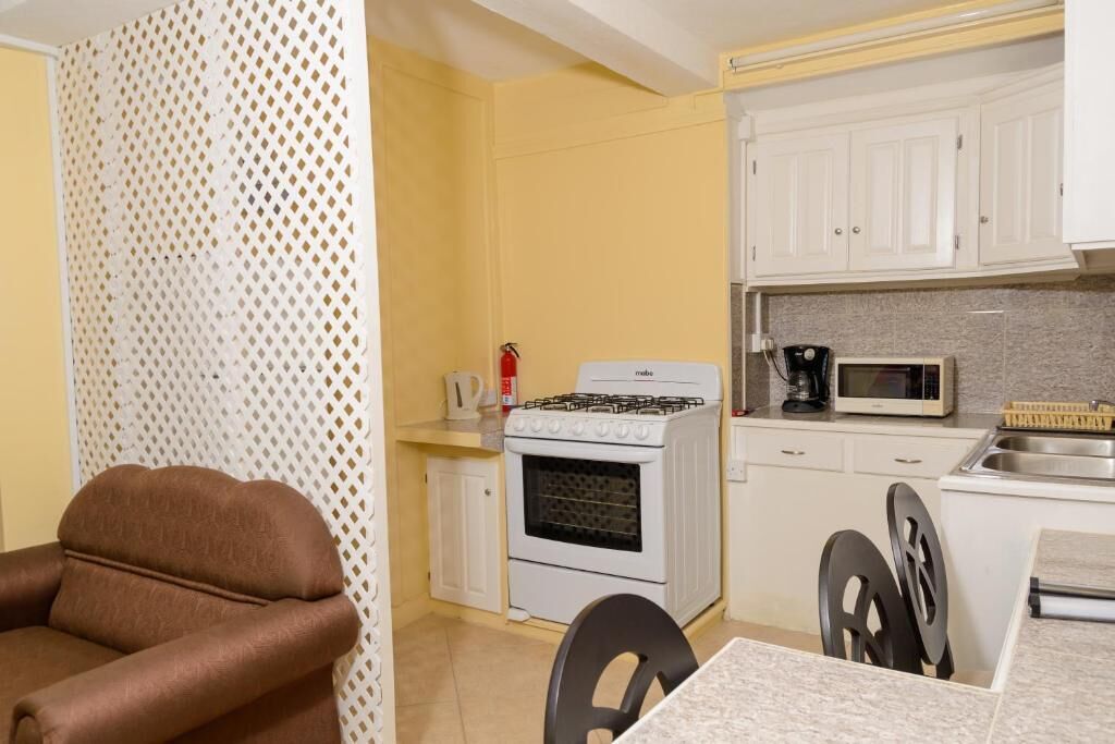 Cocina compacta con gabinetes blancos, estufa a gas, microondas y un lavamanos.