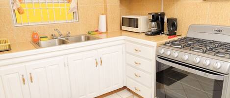 Una cocina con gabinetes blancos, estufa a gas, microondas y cafetera.
