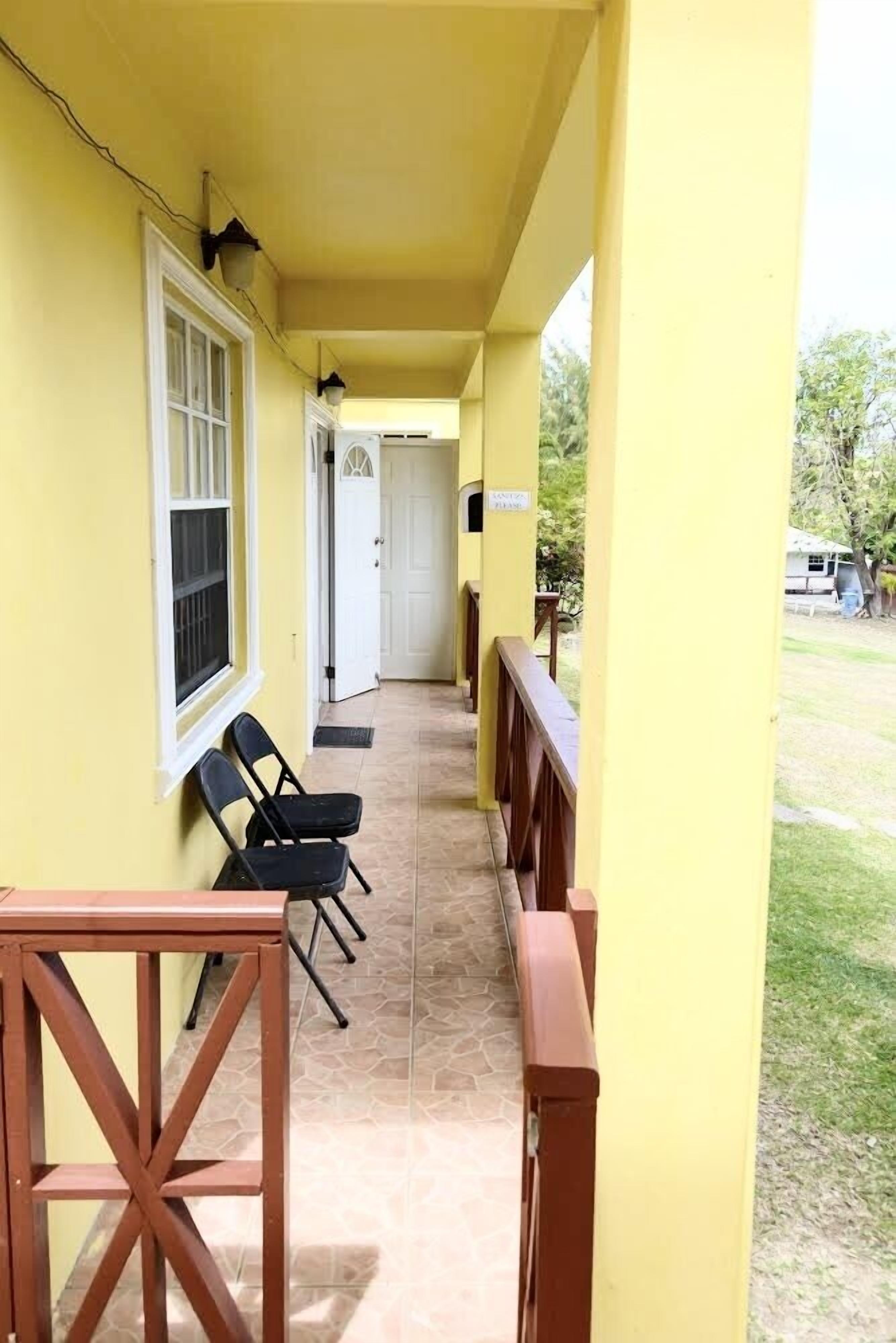 A yellow exterior corridor with a door, a window, and two black chairs.