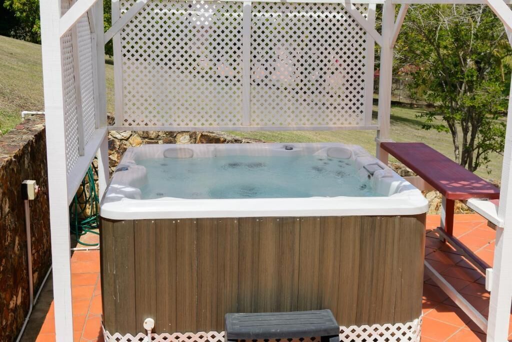 A hot tub in a wooden enclosure with a white lattice roof, surrounded by a wooden deck and a white fence.