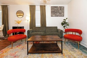 Un salon comprenant un canapé, deux fauteuils, une table basse, une lampe, un miroir et un tableau.