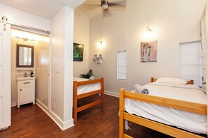 Une chambre avec deux lits superposés en bois, une commode blanche, un miroir, un tableau et un ventilateur de plafond.
