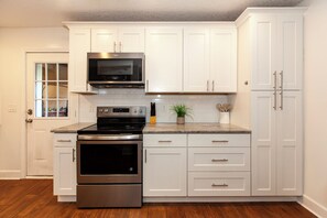 A kitchen with white cabinets, a stainless steel oven, a microwave, and a countertop with a plant and utensils. - Stylish 4BR Jacksonville Home , Sleeps 8 (Jacksonville)