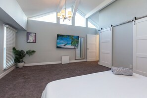 A bedroom with a large bed, a painting, a potted plant, and a sliding door.
