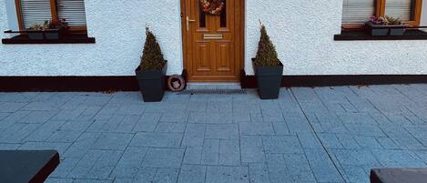 A house with a white exterior, a wooden front door with a decorative glass panel, and two potted plants on either side of the door.