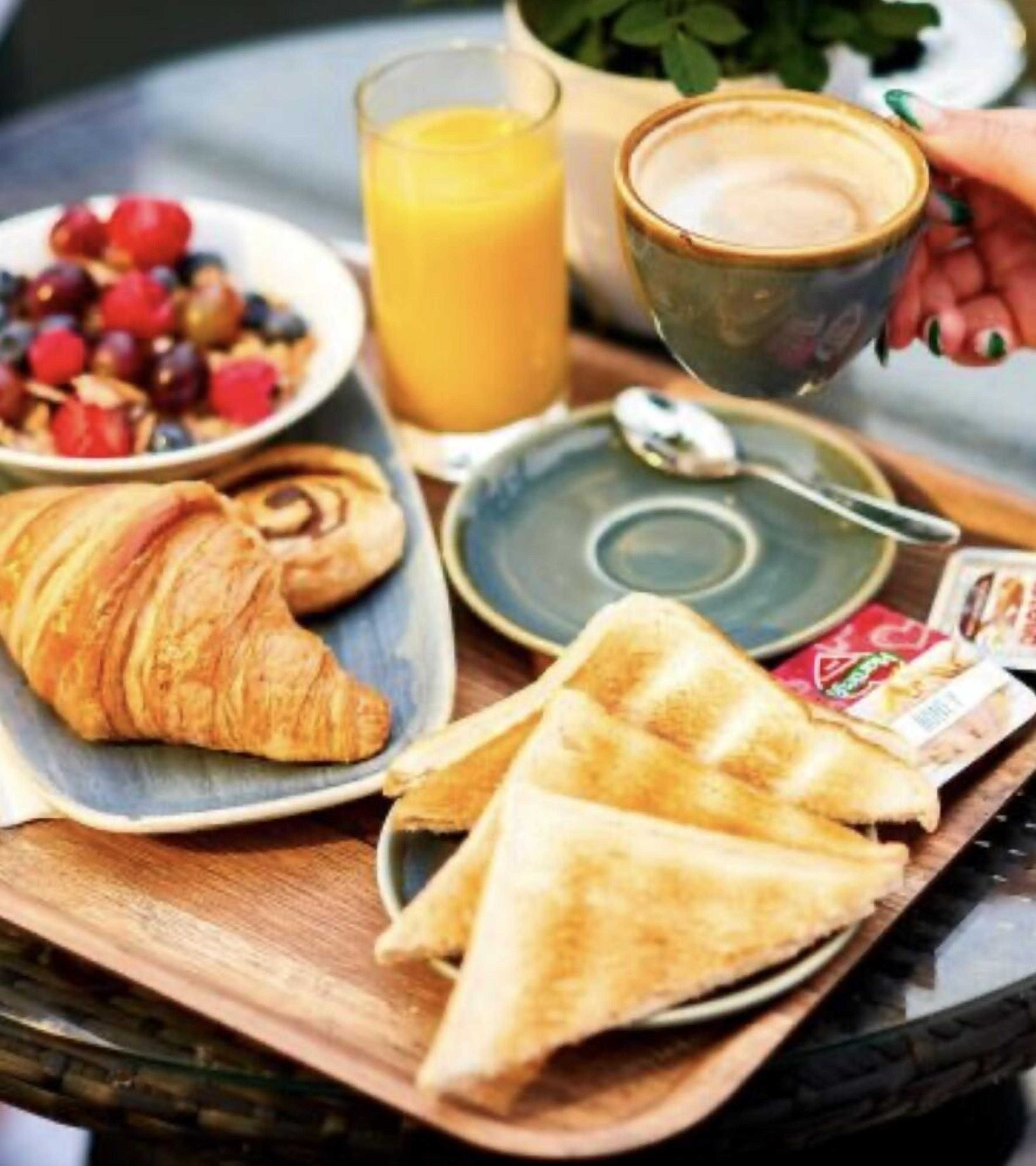 A breakfast tray with croissants, toast, a glass of orange juice, and a cup of coffee.