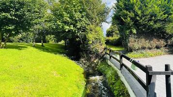 Ein Park mit einer Rasenfläche, einem kleinen Bach und einer Holzbrücke.