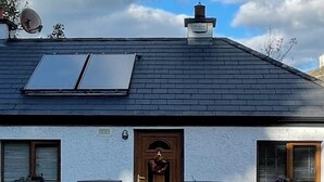 Una casa de fachada blanca, techo oscuro y dos paneles solares en el techo.