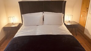 Una cama impecablemente vestida con sábanas blancas y un cabecero oscuro, flanqueada por dos mesitas de noche con lámparas.