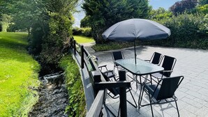Un patio al aire libre con mesa y sillas, rodeado de follaje y árboles.