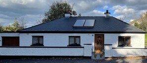 A white building with a dark roof, a satellite dish, and a door with a small porch. - River Cottage. Traditional Irish Cottage in Mullingar Ireland (Mullingar)