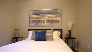 A neatly made bed with white linens and a blue pillow with the word "REST." in the center.