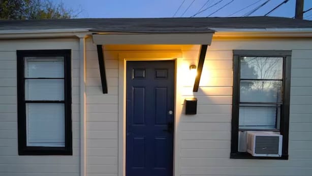 A house with a dark blue front door, a small porch, and an air conditioning unit on the right side.