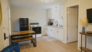 A compact kitchen with white cabinets, a black refrigerator, a stove, and a dining table with benches.