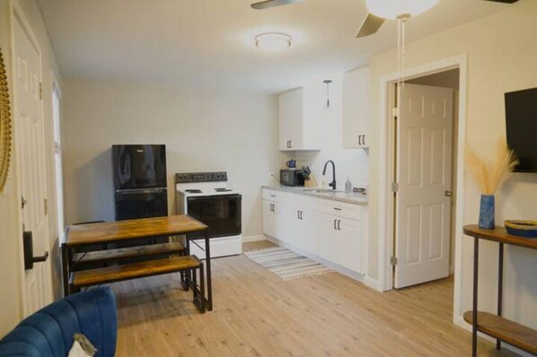 A compact kitchen with white cabinets, a black refrigerator, a stove, and a dining table with benches. - Casa Azul at La Hacienda
(Wichita Falls)