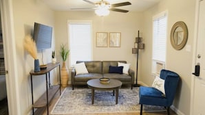 A living room with a sofa, a coffee table, a blue armchair, a floor lamp, and a ceiling fan.