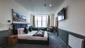 Una habitación de hotel con cama, escritorio, silla, televisor y ventana.